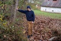 Handsome young man leans on tree on autumn trail by stone cottage