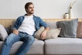 Handsome young man looking thoughtful while sitting on the couch at home Royalty Free Stock Photo