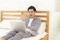 Handsome young man lying on the bed and using laptop for video chat, and waving greetings to the screen Royalty Free Stock Photo