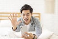 Handsome young man  lying on the bed, using a mobile phone to make a video call, and waving to the screen to greet each other Royalty Free Stock Photo