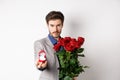 Handsome young man making a marriage proposal, stretch out hand with engagement ring and holding red roses, asking to Royalty Free Stock Photo