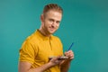 Handsome young man making notes in planner, guy holding pen, reflects on plans. Guy in yellow wear makes records in Royalty Free Stock Photo