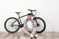 Handsome young man with modern bicycle near brick wall indoors Royalty Free Stock Photo