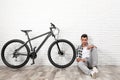 Handsome young  with modern bicycle near white brick wall indoors Royalty Free Stock Photo