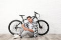 Handsome young man with  bicycle near white brick wall indoors Royalty Free Stock Photo