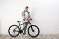 Handsome  man with modern bicycle near white brick wall indoors Royalty Free Stock Photo