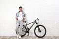 Handsome young man  modern bicycle near white brick wall indoors Royalty Free Stock Photo