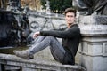 Handsome young man outdoors, sitting on old stone balusters