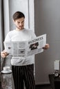 Handsome young man in pajamas reading business newspaper