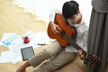 Handsome young man playing guitar while sitting on floor in living room. Royalty Free Stock Photo