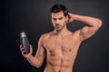 Handsome young man . Portrait of shirtless muscular man is standing on grey background with shampoo in hand. Men care