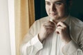 Handsome young man preparing for business meeting, putting on shirt, happy groom posing near window in hotel room before the Royalty Free Stock Photo