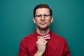 Handsome young man in a red shirt correcting bow-tie against a green background