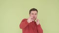 Handsome young man in a red sweater funny shows shots from a gun with his hands isolated