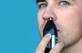 Handsome young man remove hair from his nose with trimmer