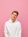 Handsome young man in roe deer stands on a pink background, looks into the camera and smiles, wearing a white hoodie. Positive Royalty Free Stock Photo