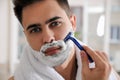 Handsome young man shaving with razor in bathroom Royalty Free Stock Photo