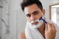 Handsome young man shaving with razor in bathroom, space for text Royalty Free Stock Photo