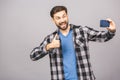 Handsome young man in shirt holding camera and making selfie and smiling while standing against grey background Royalty Free Stock Photo