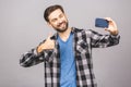 Handsome young man in shirt holding camera and making selfie and smiling while standing against grey background Royalty Free Stock Photo