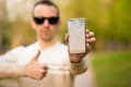 Handsome young man showing broken smartphone screen doing ok sign, thumb up with fingers