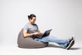 Handsome young man sitting on a bean bag putting his laptop on his legs and working isolated on white background