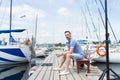 Handsome young man sitting on bench in dock of the bay between boats. man on pier looking away. Royalty Free Stock Photo