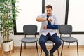 Handsome young man sitting at doctor waiting room with arm injury looking at the watch time worried, afraid of getting late Royalty Free Stock Photo