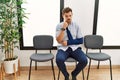 Handsome young man sitting at doctor waiting room with arm injury pointing to the eye watching you gesture, suspicious expression Royalty Free Stock Photo