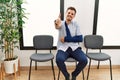 Handsome young man sitting at doctor waiting room with arm injury smiling friendly offering handshake as greeting and welcoming Royalty Free Stock Photo