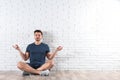 Handsome young man sitting on floor and practicing zen yoga near brick wall Royalty Free Stock Photo