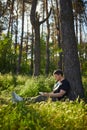 Handsome young man sitting in the forest on the grass reading a book Royalty Free Stock Photo