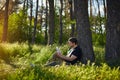 Handsome young man sitting in the forest on the grass reading a book Royalty Free Stock Photo