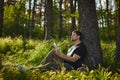 Handsome young man sitting in the forest on the grass reading a book Royalty Free Stock Photo