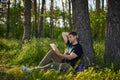 Handsome young man sitting in the forest on the grass reading a book Royalty Free Stock Photo