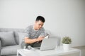 Handsome Young Man Sitting on the Living Room Couch, Writing Some Notes While Looking at his Laptop Computer Royalty Free Stock Photo