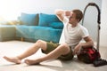 Handsome young man sitting near vacuum cleaner in the living room looking tired after cleaning appartment house chores Royalty Free Stock Photo