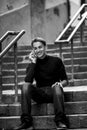 A handsome young man sitting on the steps on a narrow street talking on his cell phone. Royalty Free Stock Photo