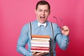 Handsome young man with stack of books looking at camera and screaming while standing on rosy background. Tired student finds out