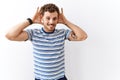 Handsome young man standing over isolated background trying to hear both hands on ear gesture, curious for gossip Royalty Free Stock Photo