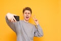 Handsome young man standing on a yellow background and posing on a smartphone camera. Handsome young man doing a selfie and posing Royalty Free Stock Photo