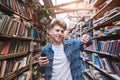 Handsome young man stands in a library with a smearphone in his hand and shows his finger down Royalty Free Stock Photo