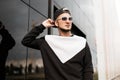 Handsome young man straightens black baseball cap. Attractive hipster guy in vintage sunglasses in trendy sweatshirt poses Royalty Free Stock Photo