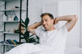 handsome young man stretching hands and smiling at camera while sitting on bed Royalty Free Stock Photo