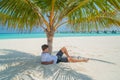 Handsome young man in stylish clothes relaxing under palm tree at tropical sandy beach at island luxury resort Royalty Free Stock Photo