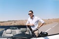 Handsome young man in sunglasses leaning on luxury white convertible while standing stop on road Royalty Free Stock Photo