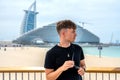 Handsome young man with sunglasses looking at seaside while standing near fence at beach in Dubai. Royalty Free Stock Photo