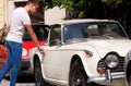 Handsome young man in sunglasses standing in urban city street next to an old retro car. A guy opening and entering old timer car. Royalty Free Stock Photo