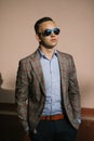 Handsome young man in sunglasses stands against the wall.