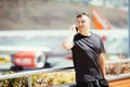 Handsome young man talking on the phone is standing at terrace in airport terminal while waiting for the flight with plane on back Royalty Free Stock Photo